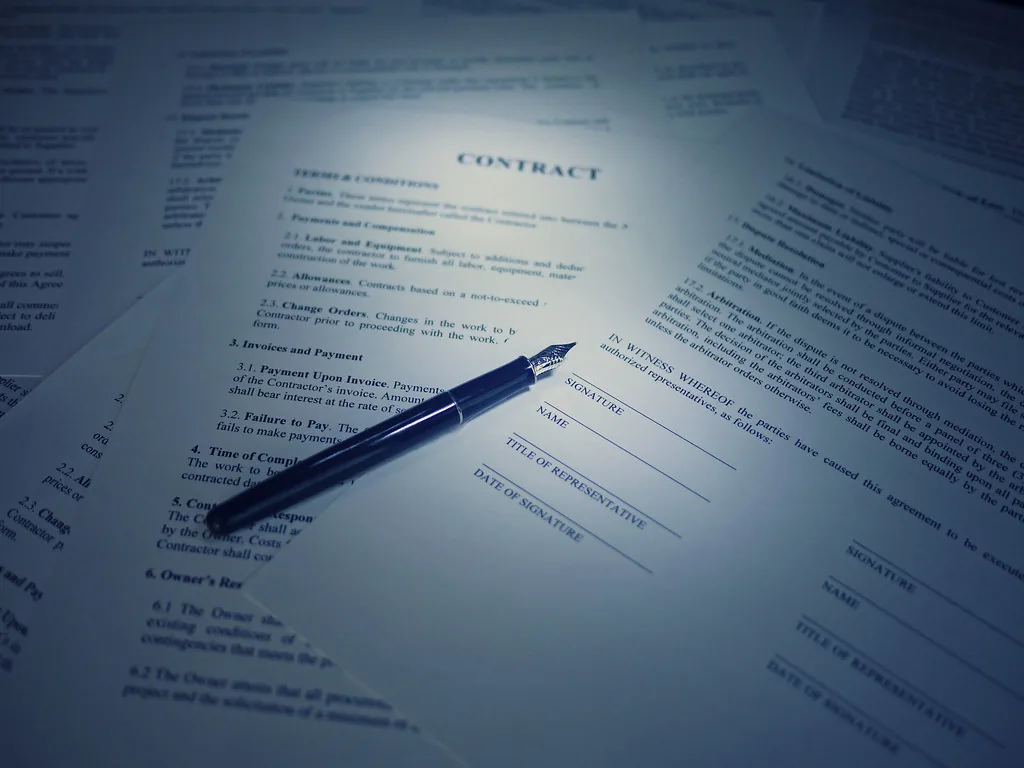 A policy contract on a desk with a pen resting on the signature page