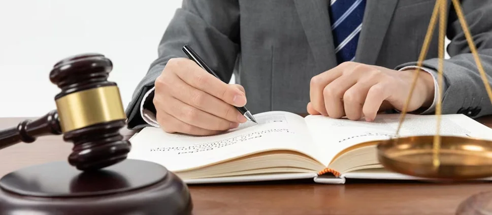 A lawyer making notes in a law book, beside a gavel and a set of brass scales