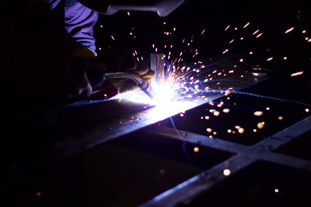 A welder at work on a factory floor, sparks rising from the joint