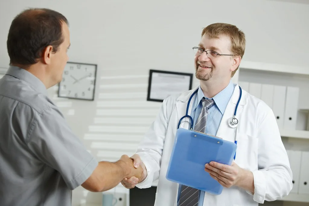 A doctor greeting a patient with a handshake in a clinic office