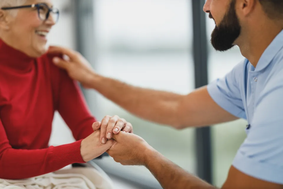 A caregiver holding an elderly woman’s hands during a home visit