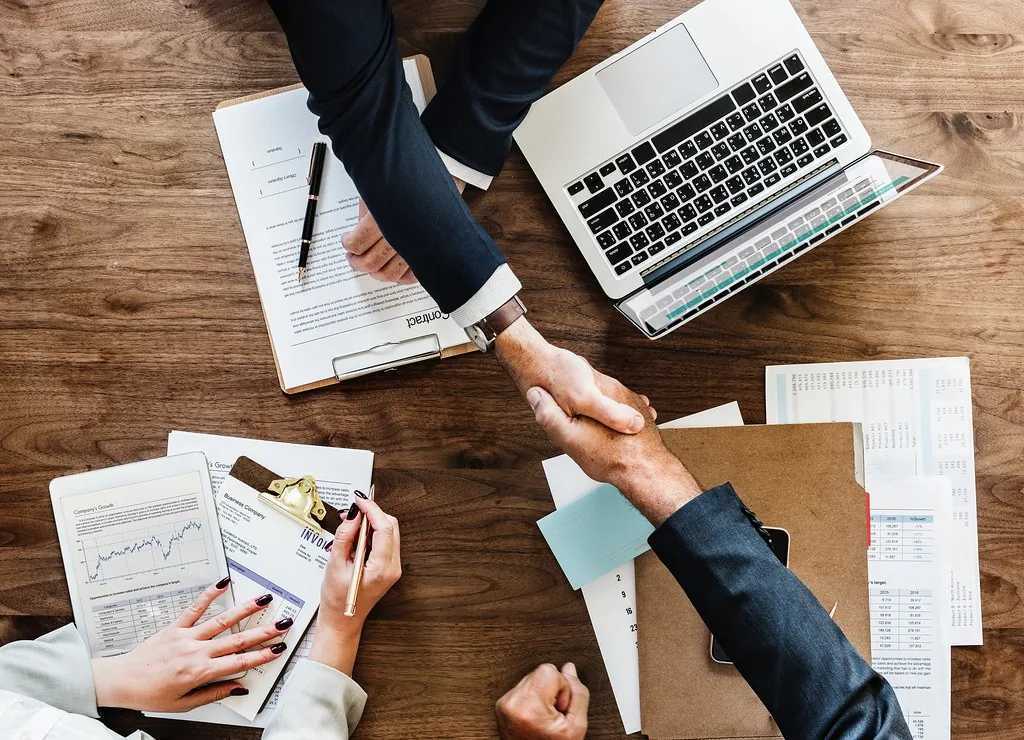 A handshake across a desk of resumes and offer paperwork
